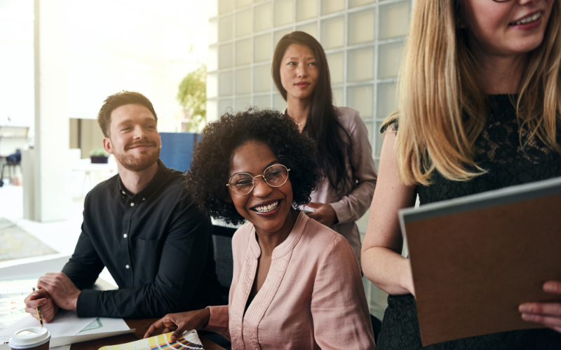 A group of four people in business casual attire are engaged in a discussion in a bright, modern office setting.