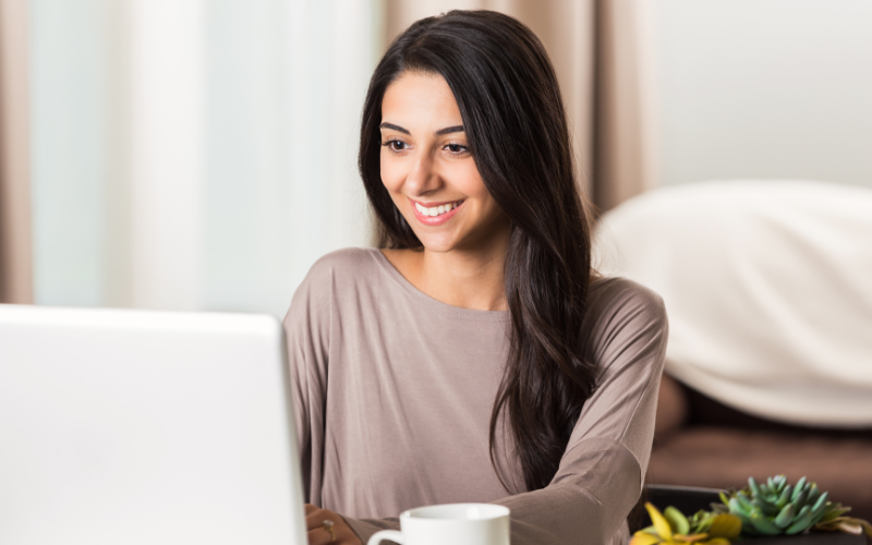 Woman with long dark hair sitting at a desk, smiling at a laptop participating in Telehealth.