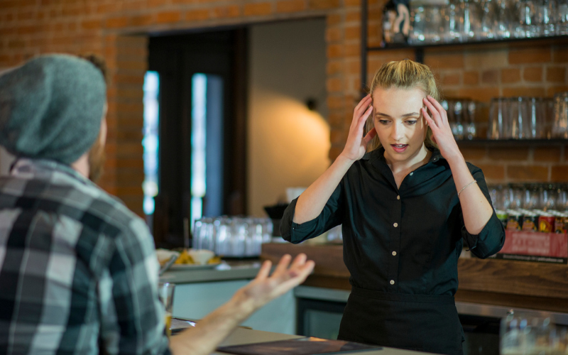 A waitress appears stressed while speaking to a customer at a restaurant counter.