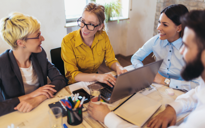 Four employees engaged in a positive discussion around a table with a laptop, documents, and stationery.