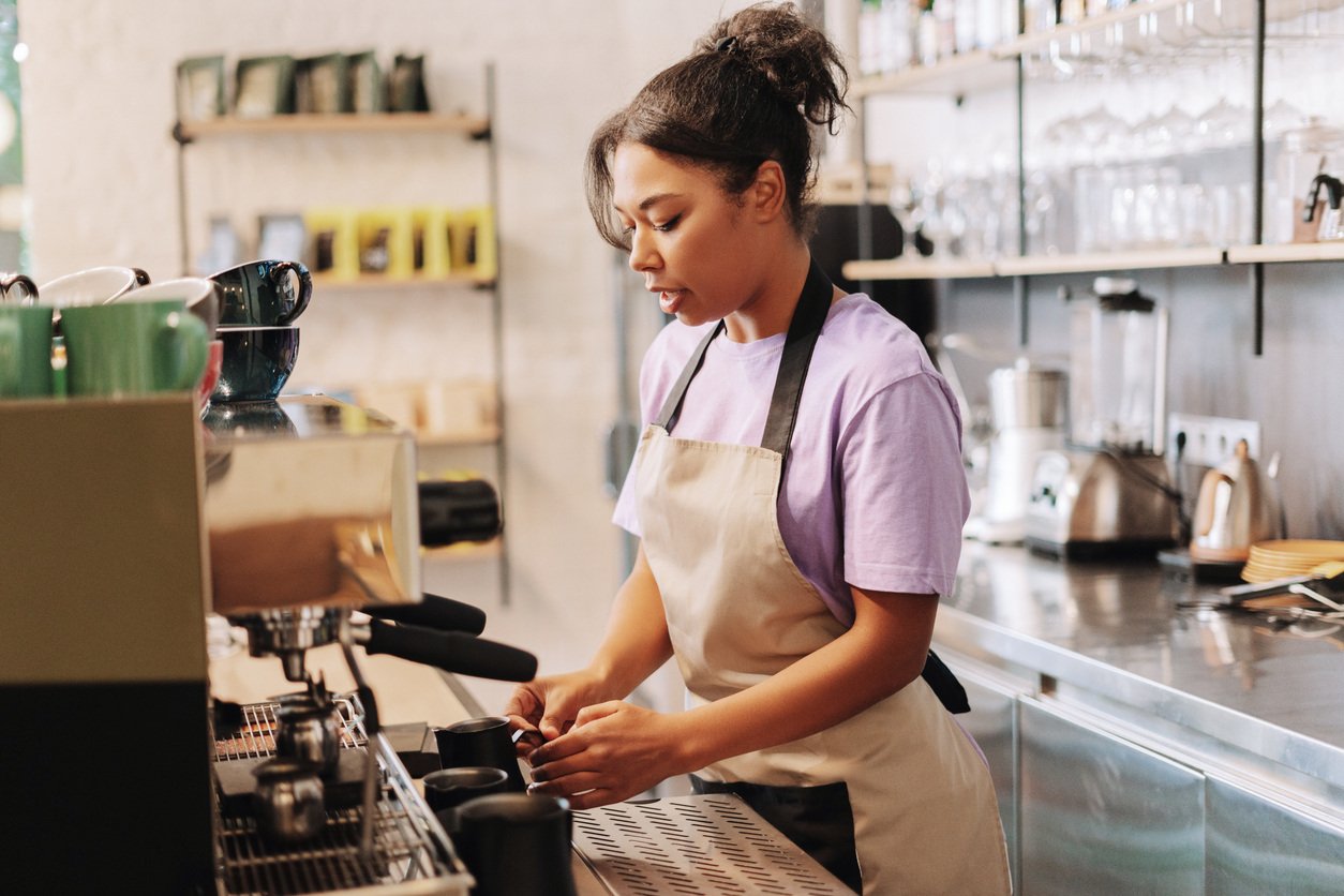 An employee prepares coffee behind a counter in a cafe. 